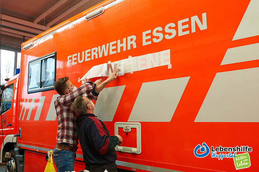 Mitarbeiter der Lebenshilfe Wuppertal beschriften einen Essener Feuerwehrwagen.