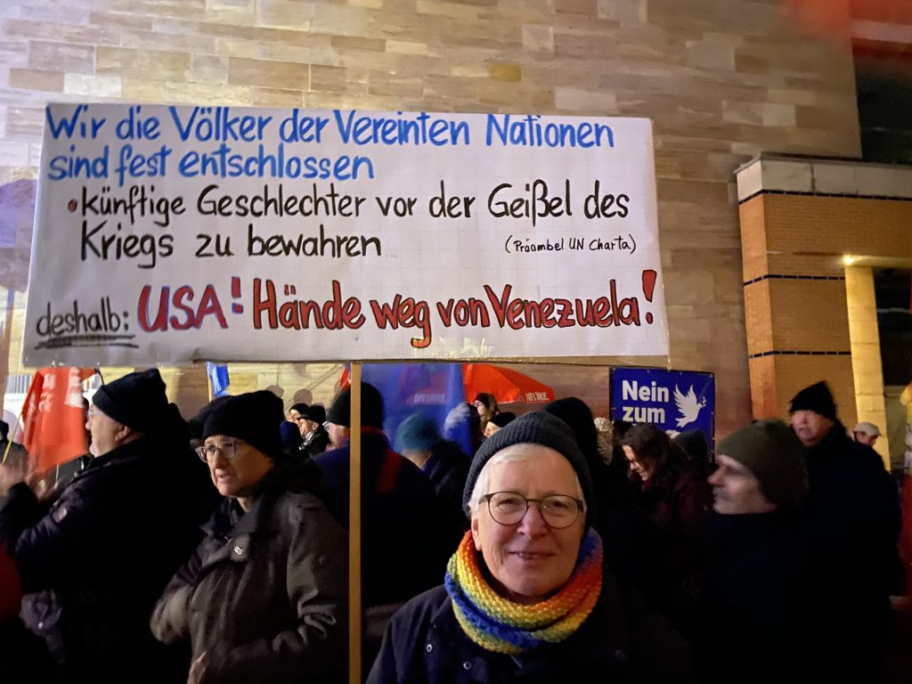 Foto: Ein Demonstrant hält ein Plakat mit dem Text "Wir, die Völker der Vereinten Nationen, sind fest entschlossen • künftige Geschlechter vor der Geißel des Krieges zu bewahren (Präambel der UN-Charta) deshalb: USA! Hände weg von Venezuela!