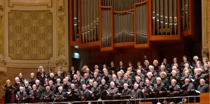 Der Chor steht auf einem Chorpodium. Im Hintergrund ist eine große Orgel zu sehen